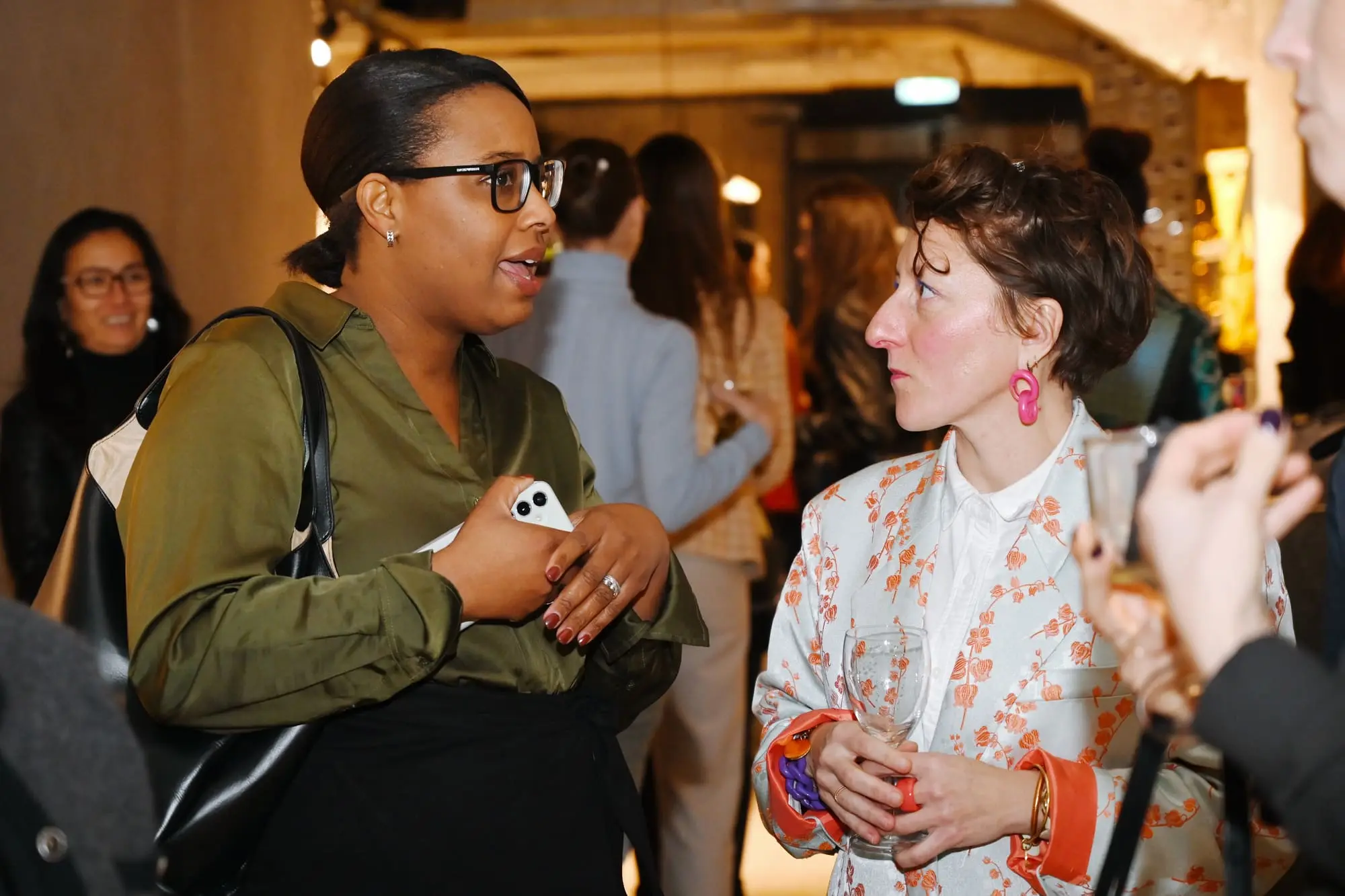 Two women in animated conversation at a Next Women reception, other guests around them
